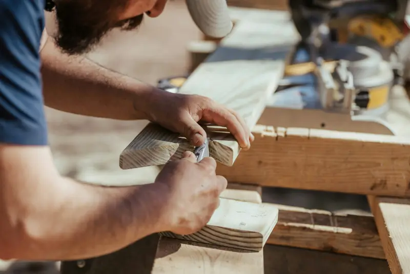 A carpenter marking a cut on a board next to a miter saw